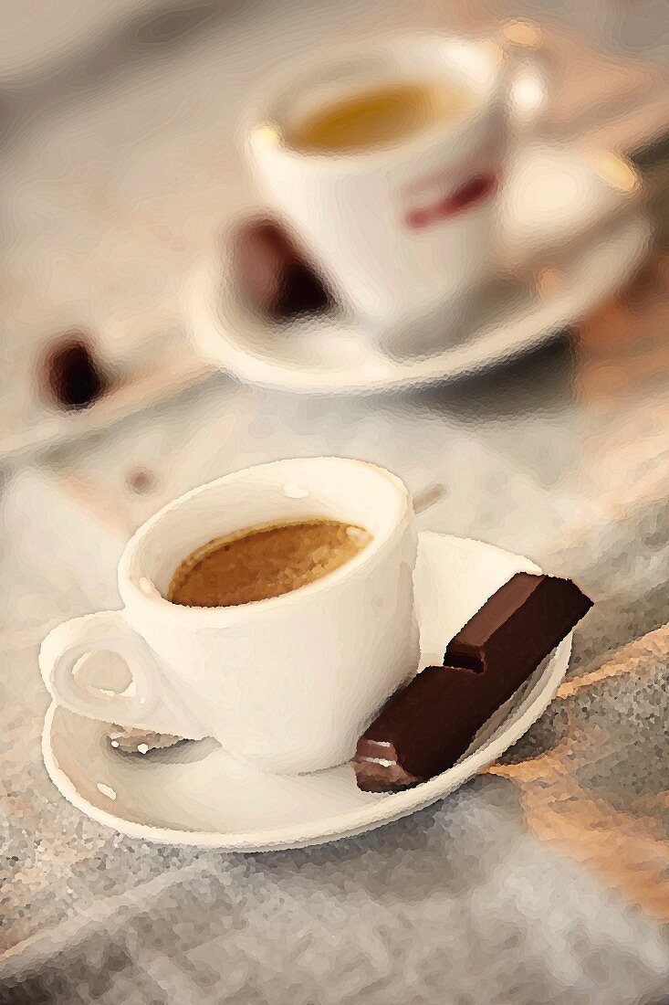 Two cups of espresso served with a piece of dark chocolate
