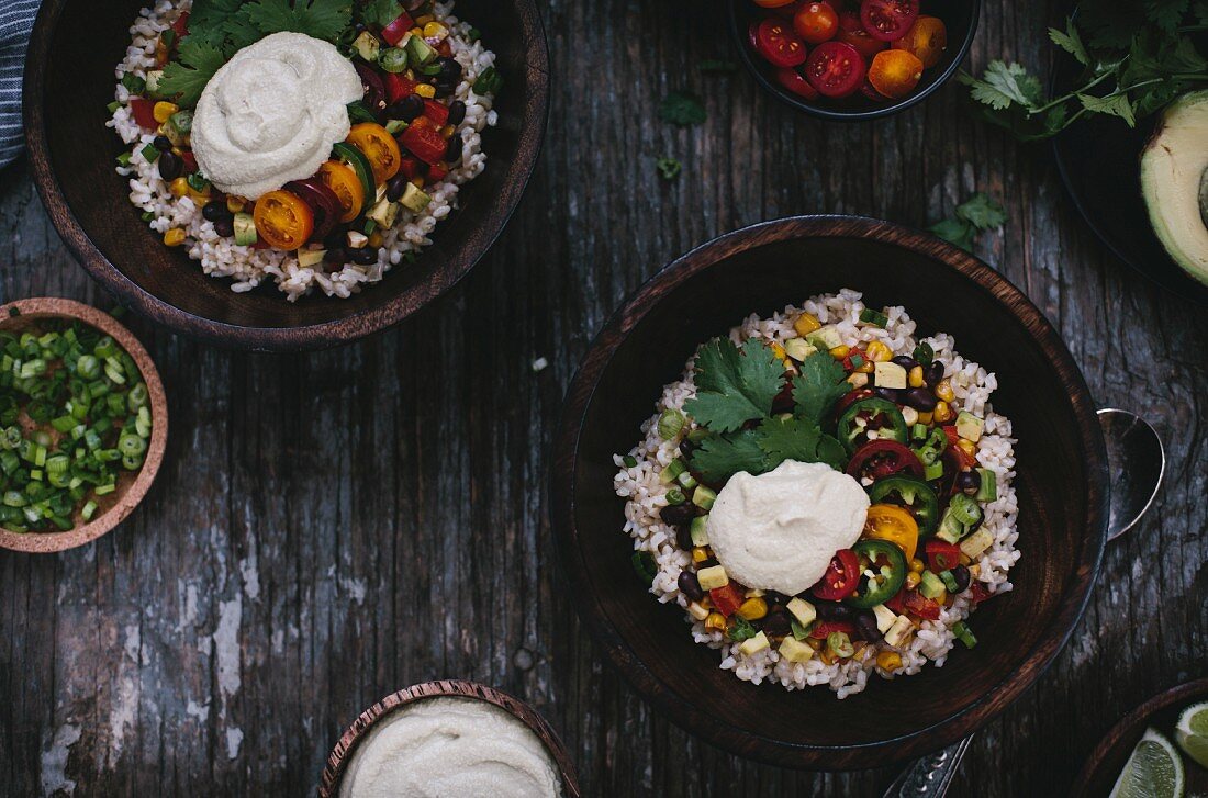Two bowls of Mexican Burrito Bowl with cashew cream sauce surrounded