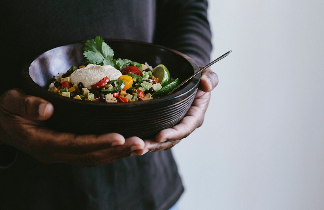 A man holding a Mexican burrito bowl topped with cashew cream sauce