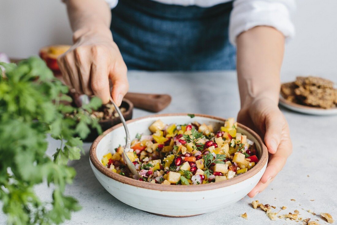 A woman mixing a bowl of peach salsa with walnuts and pomegranate seeds