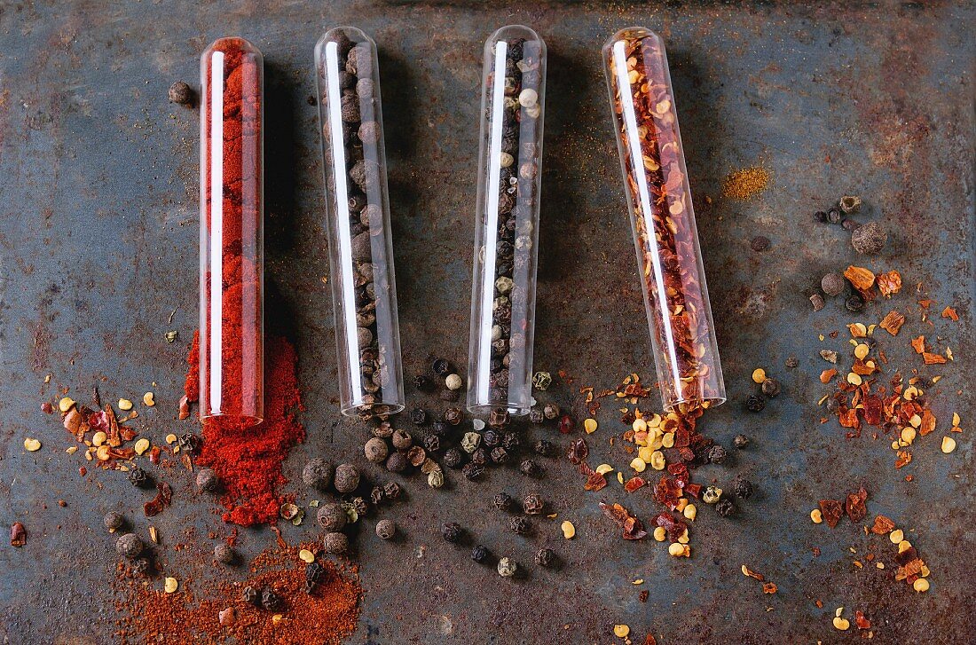 Spicy background with assortment of different hot chili and allspice peppers in glass test-tube