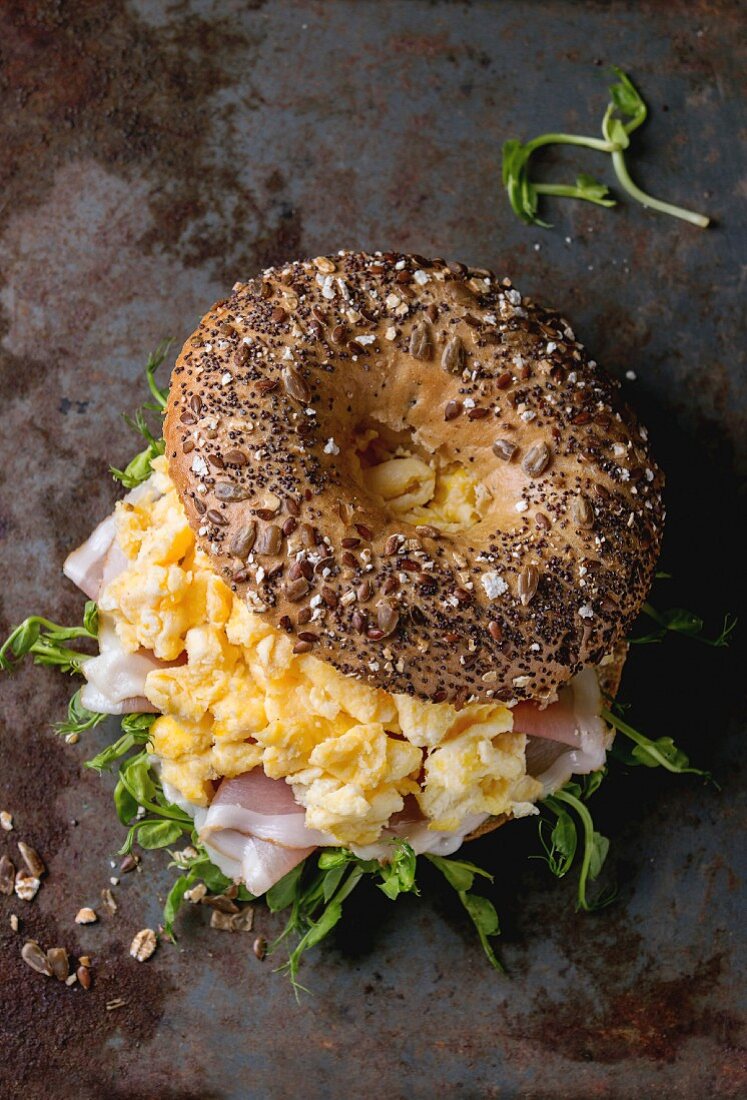 Opened Whole Grain bagels with scrambled eggs, pea sprout and prosciutto ham