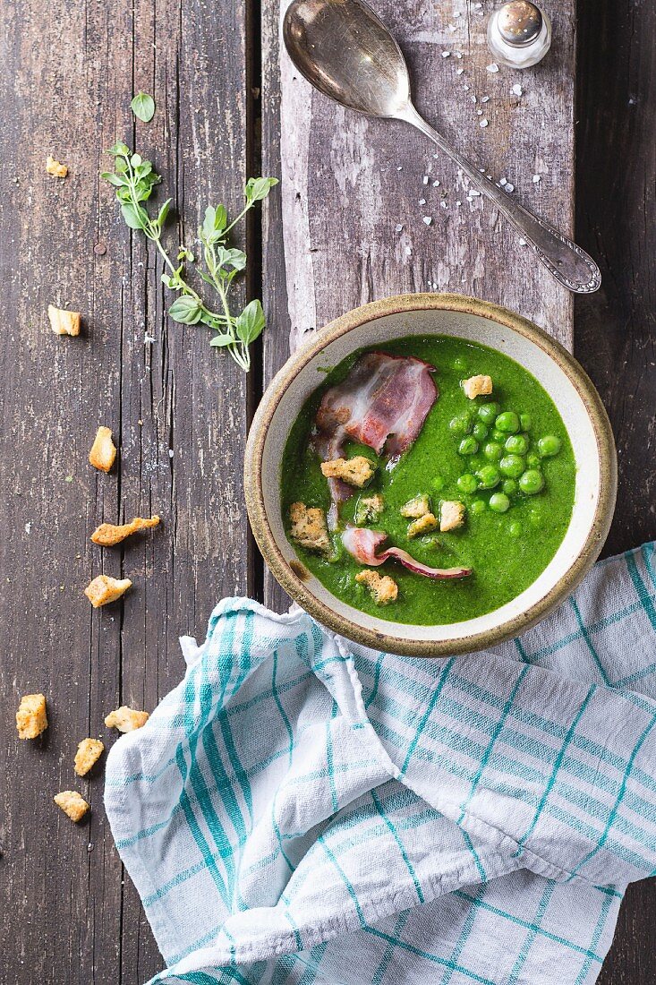 Cream soup of green peas in ceramic bowl with fried bacon and croutons