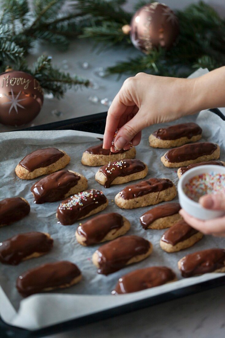 Almond and chocolate cookies on a baking tray, person putting sprinkles on the cookies