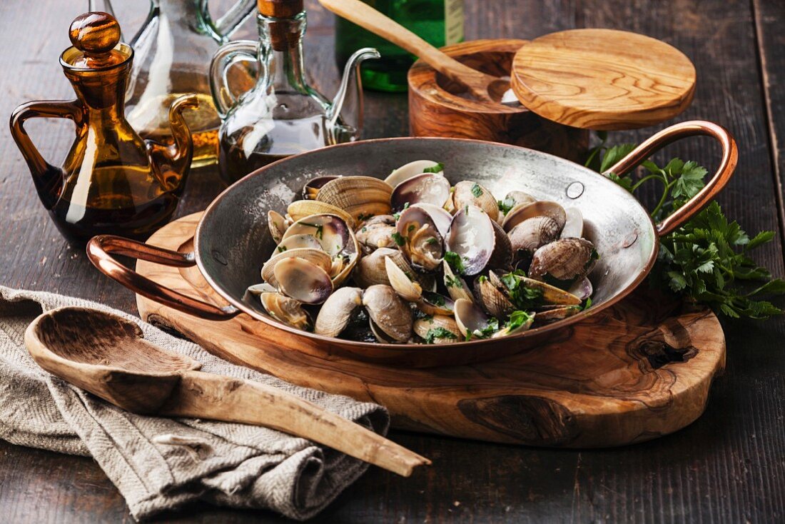 Shells vongole venus clams with parsley in copper cooking dish on dark wooden background