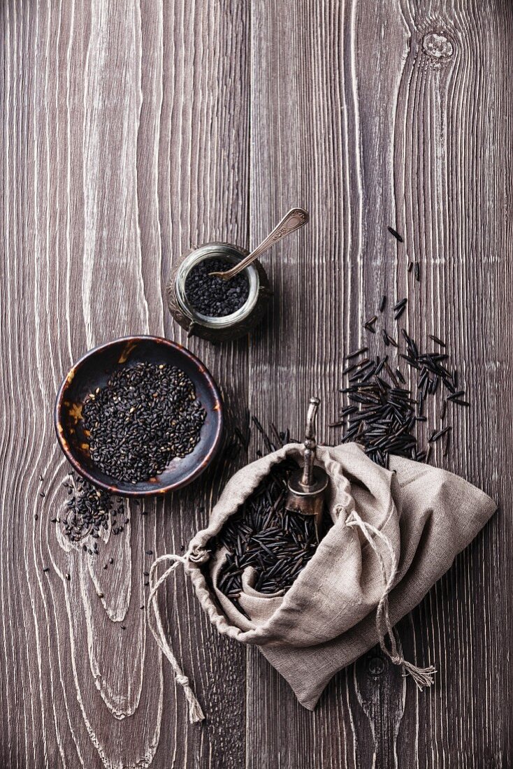 Black raw food ingredients - wild rice, sesame seeds, black salt on gray wooden background