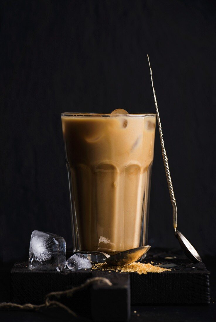 Eiskaffee mit Milch in hohem Glas vor schwarzem Hintergrund