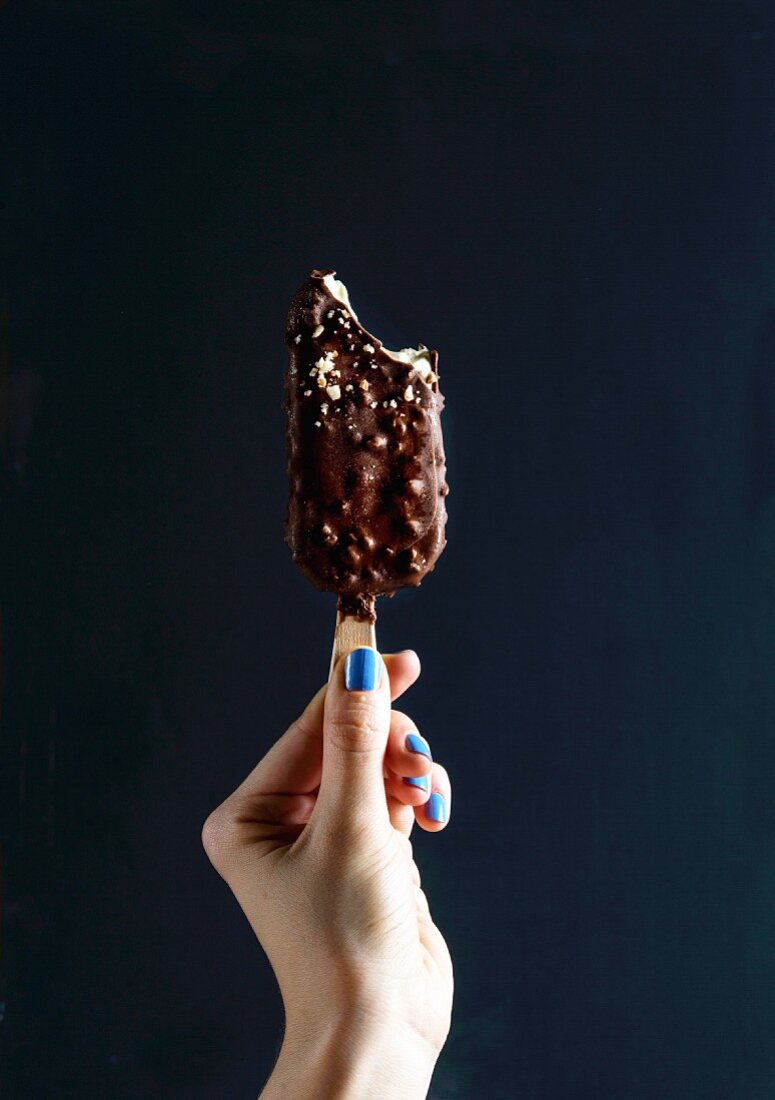 A hand holding a chocolate ice cream lollipop