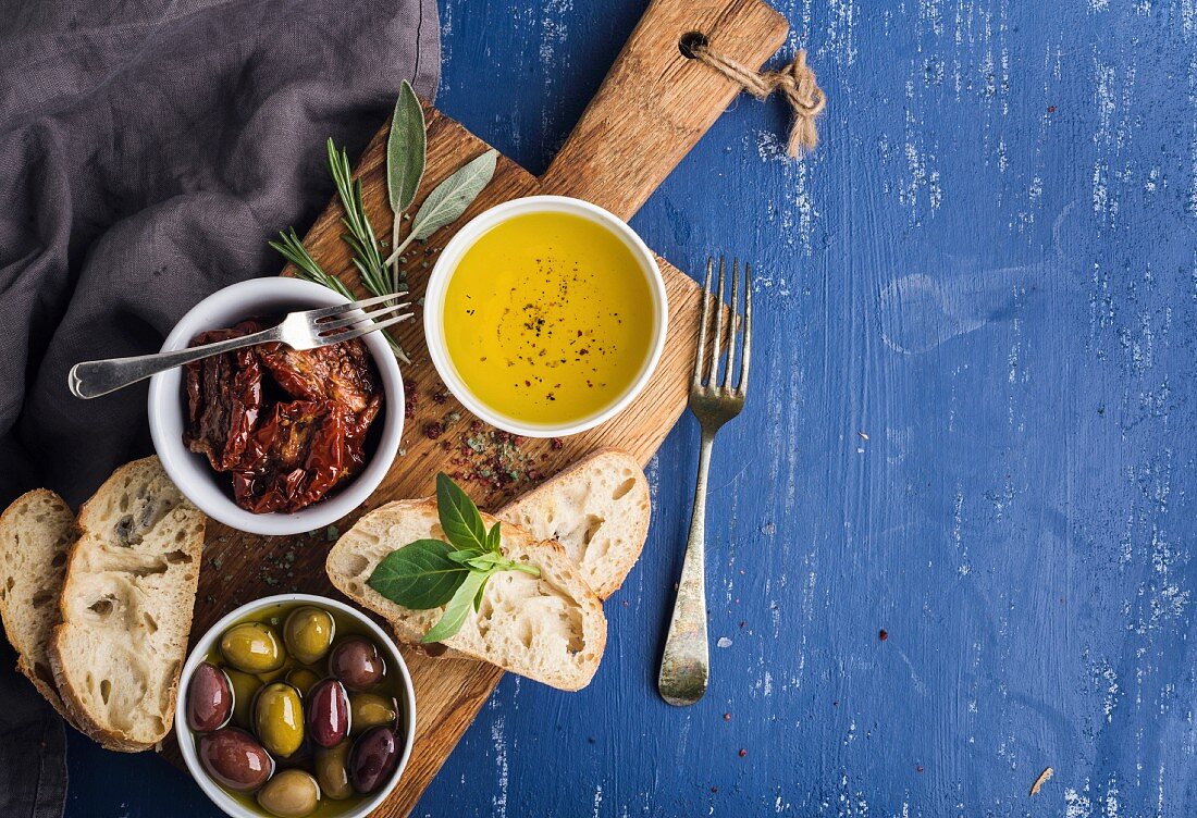 Mediterranean snacks set. Olives, oil, herbs and sliced ciabatta bread on yellow rustic oak board