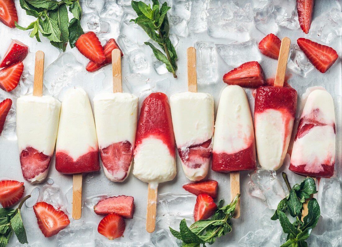 Strawberry yogurt ice cream popsicles with mint over steel tray background