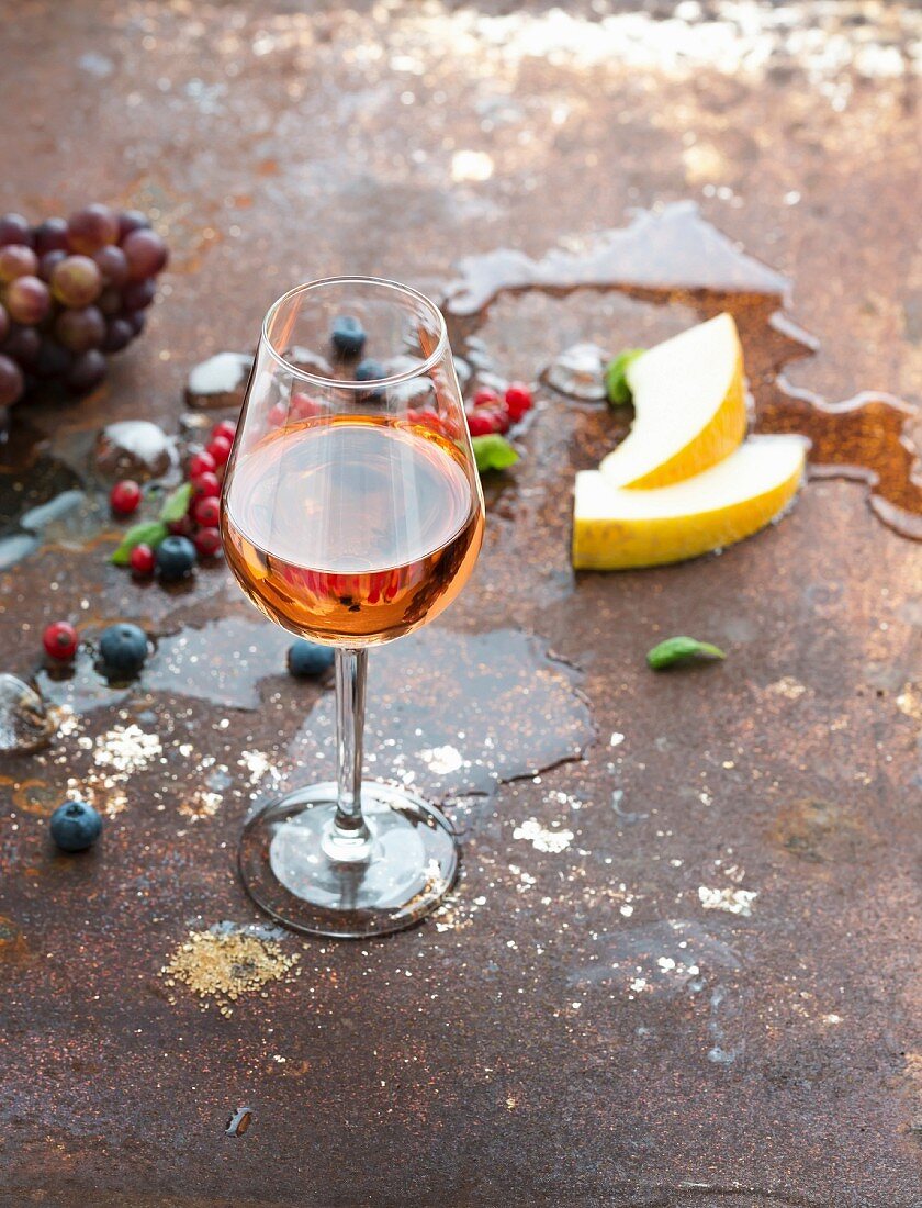 Glass of rose wine with berries, melon, grapes and ice on rusty metal background