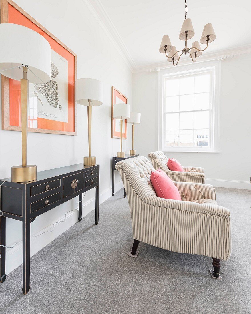 An elegant salon with two black console tables and table lamps in front of framed pictures