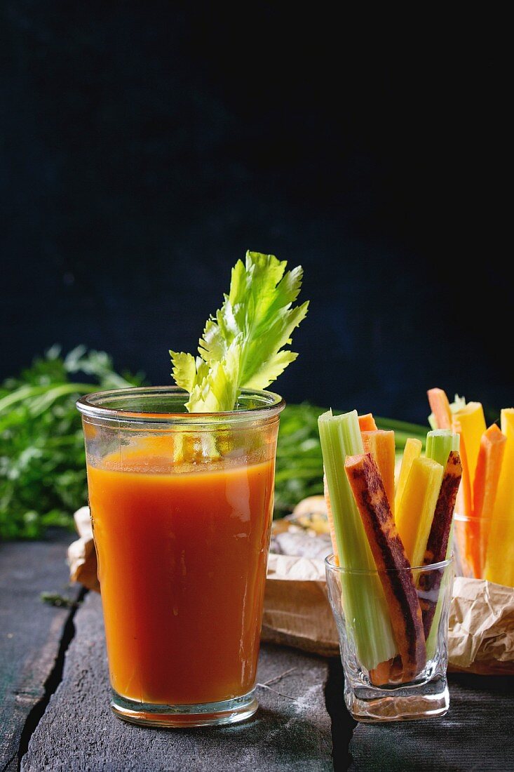 Sliced colorful raw carrots and celery as vegetarian snack, and glass cup of fresh orange and carrot juice