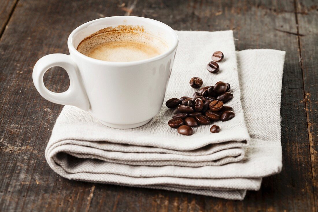 Espresso in Tasse mit Kaffeebohnen auf Holzuntergrund
