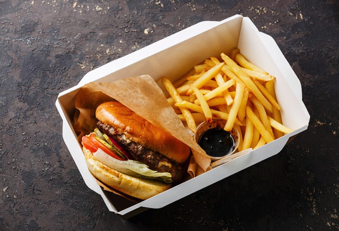 Burger und Pommes Frites in Papierschale auf dunklem Hintergrund