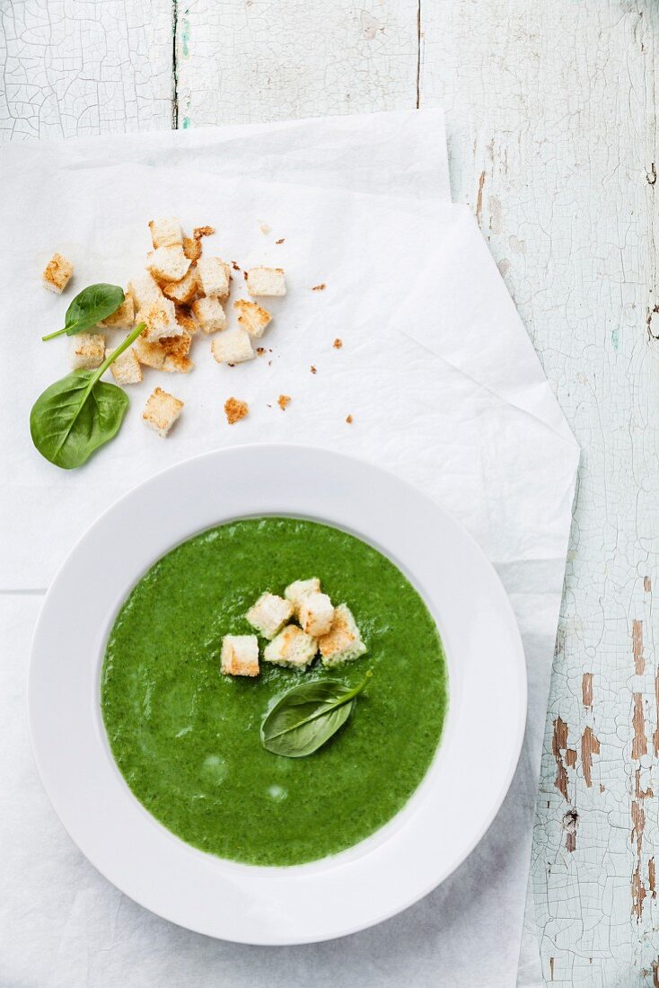 Spinach broccoli soup with croutons in white bowl