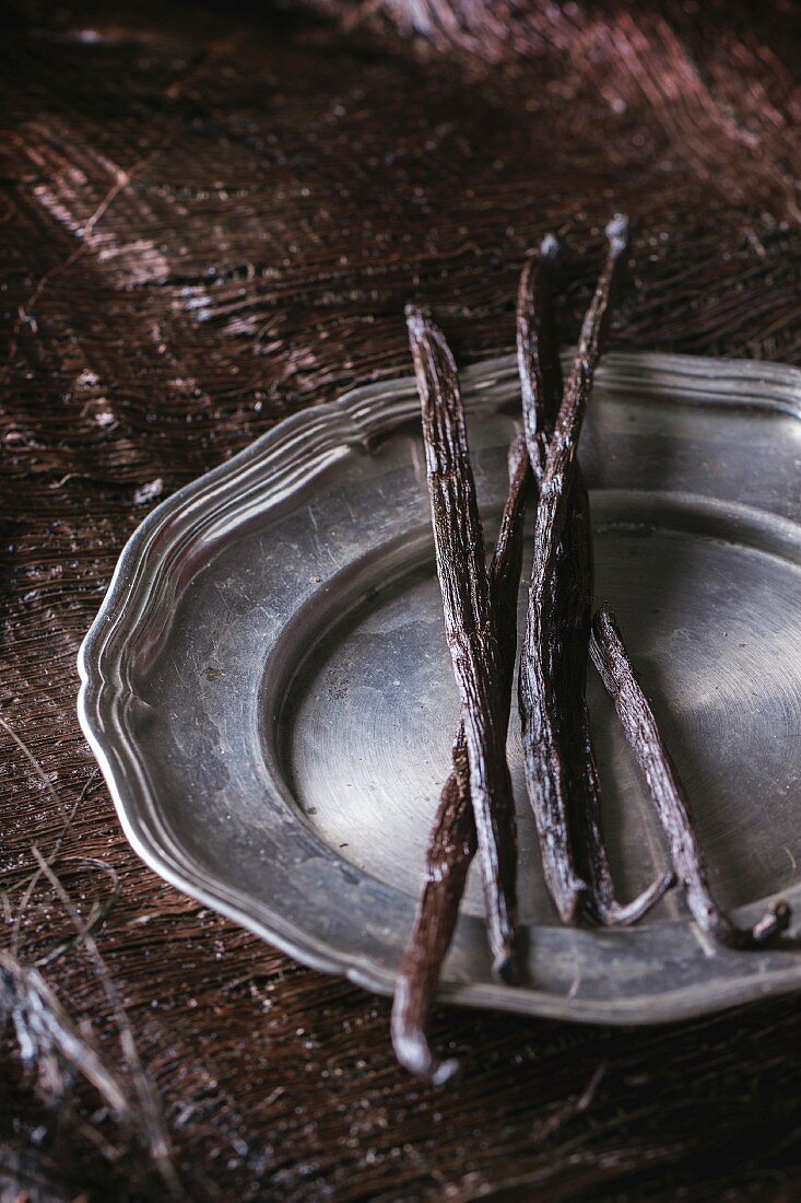 Heap of vanilla sticks in vintage metal plate over dark palm crust