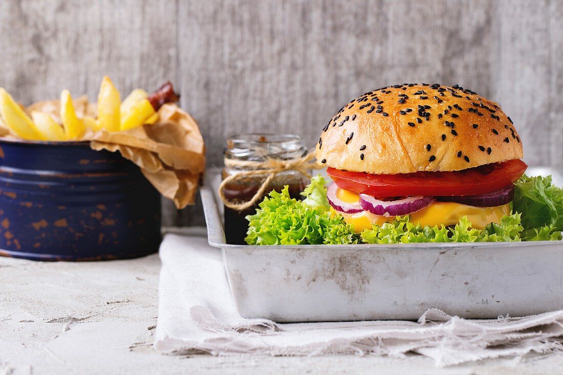 Hausgemachter Hamburger mit schwarzem Sesam Aluminiumform, dazu Pommes Frites