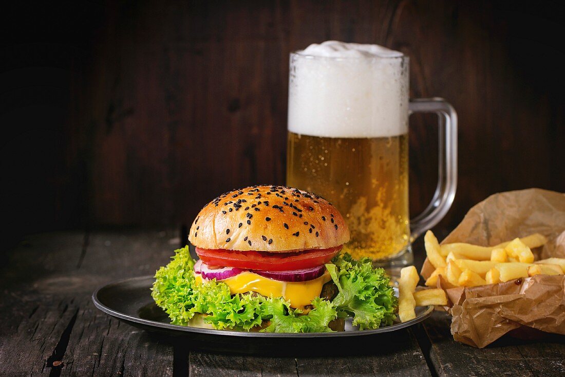 Hausgemachter Hamburger mit schwarzem Sesam, Pommes Frites und ein Glas Bier
