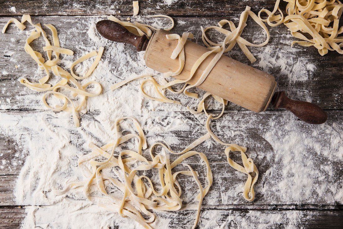 Top view on raw homemade pasta with flour and vintage rolling pin over old wooden table