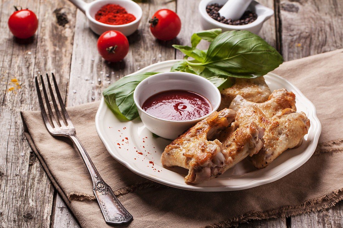 Plate of grilled chicken wings served with tomato deep and fresh basil over old wooden table