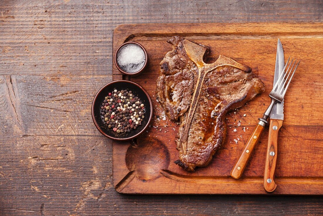 Gegrilltes T-Bone-Steak mit Salz und Pfeffer auf Schneidebrett auf Holzuntergrund