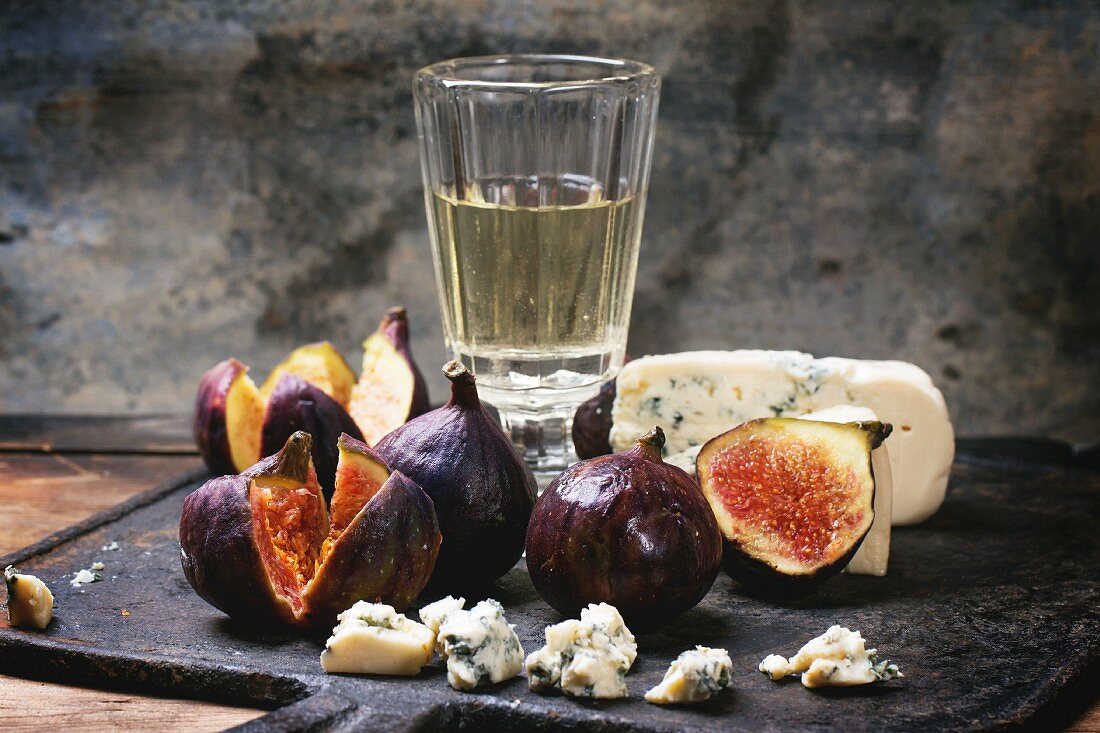 Figs with blue cheese, white wine and crackers on black cutting board