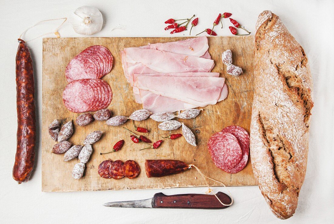 Wooden cutting board with set of ham and salami sausages with fresh bread and red hot chili peppers