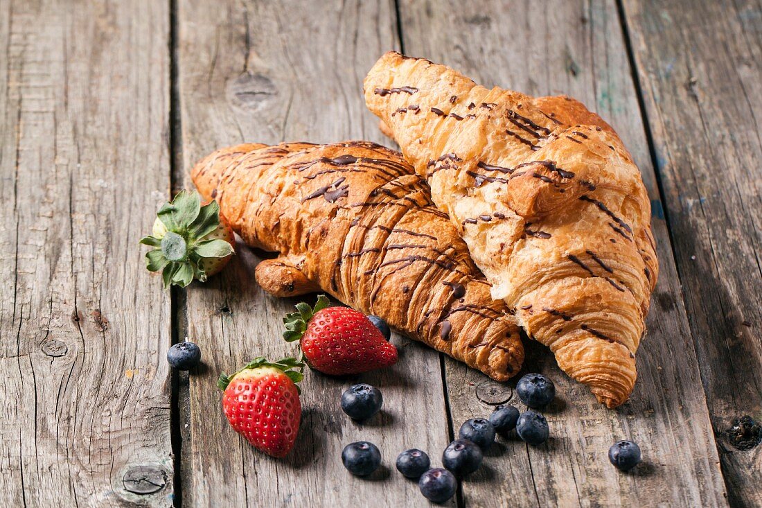 Two fresh croissant with berries over old wooden table