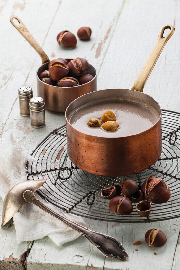 Chestnut soup in copper pot with roasted chestnuts on blue textural background