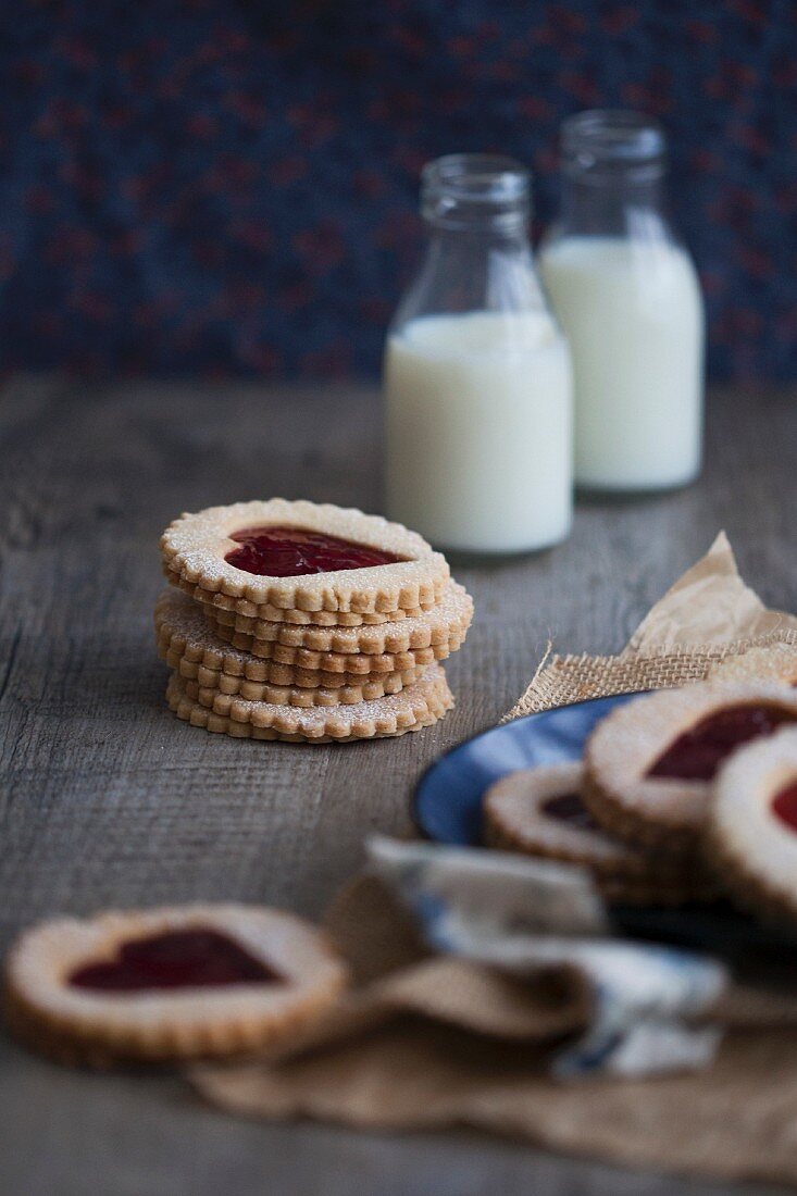 Linzer Plätzchen mit Herzmotiv und Erdbeermarmelade, im Hintergrund Milchflaschen