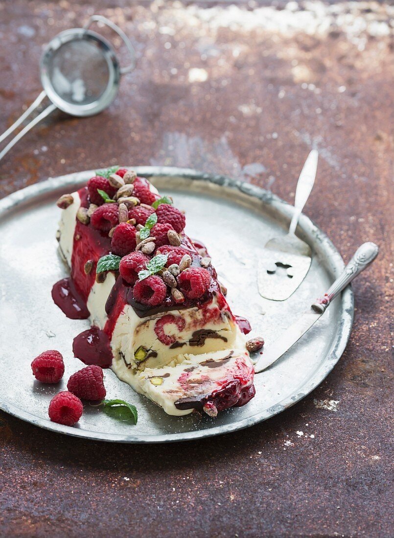 Semifreddo or italian cheese ice-cream dessert with pistachios, fresh raspberries and mint on vintage silver tray