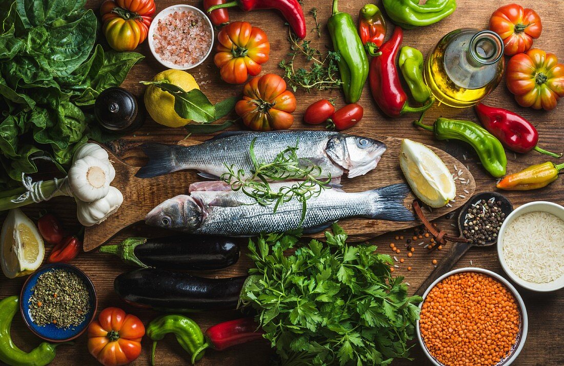 Raw uncooked seabass fish with vegetables, grains, herbs and spices on chopping board