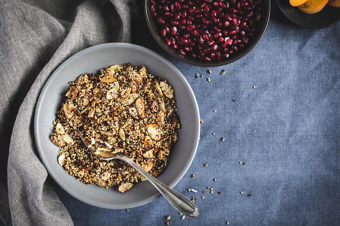 A bowl of quinoa crunch surrounded with pomegranate seeds and sliced apricots