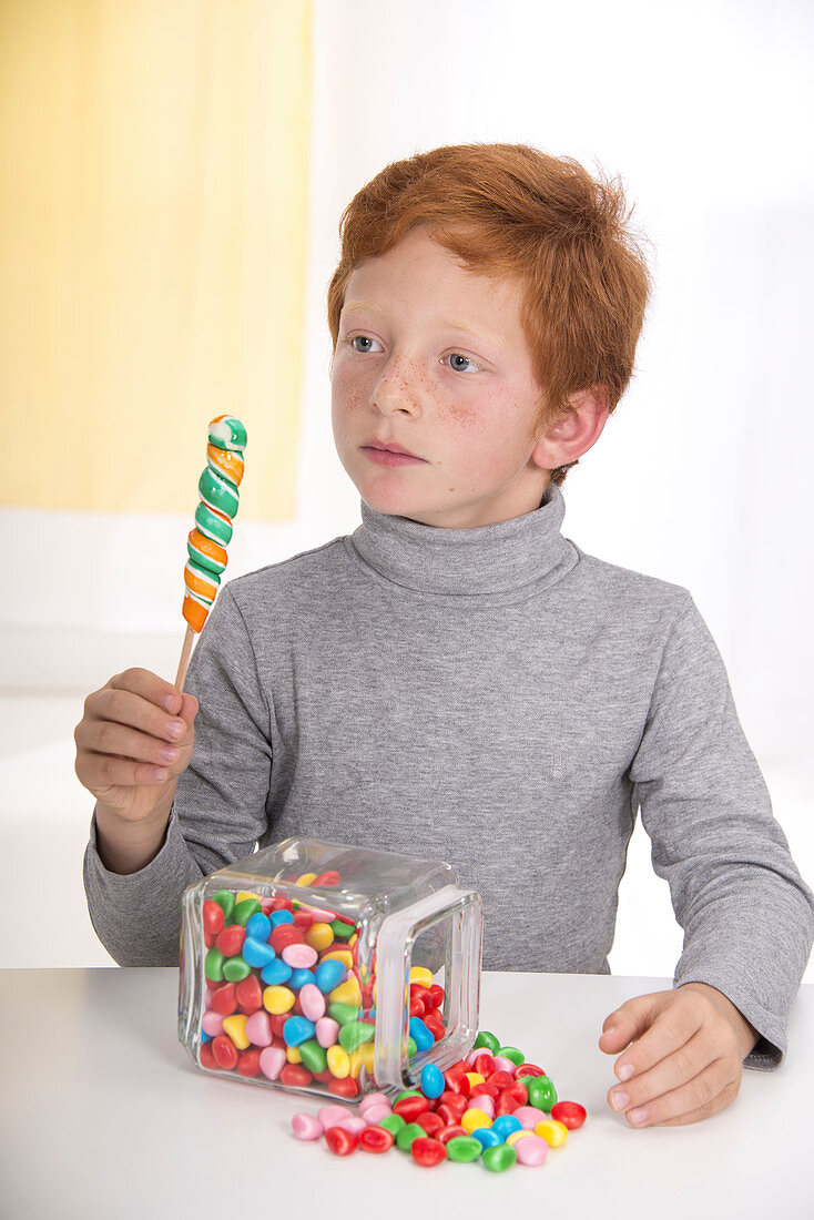 Boy holding lollipop with jar of sweets
