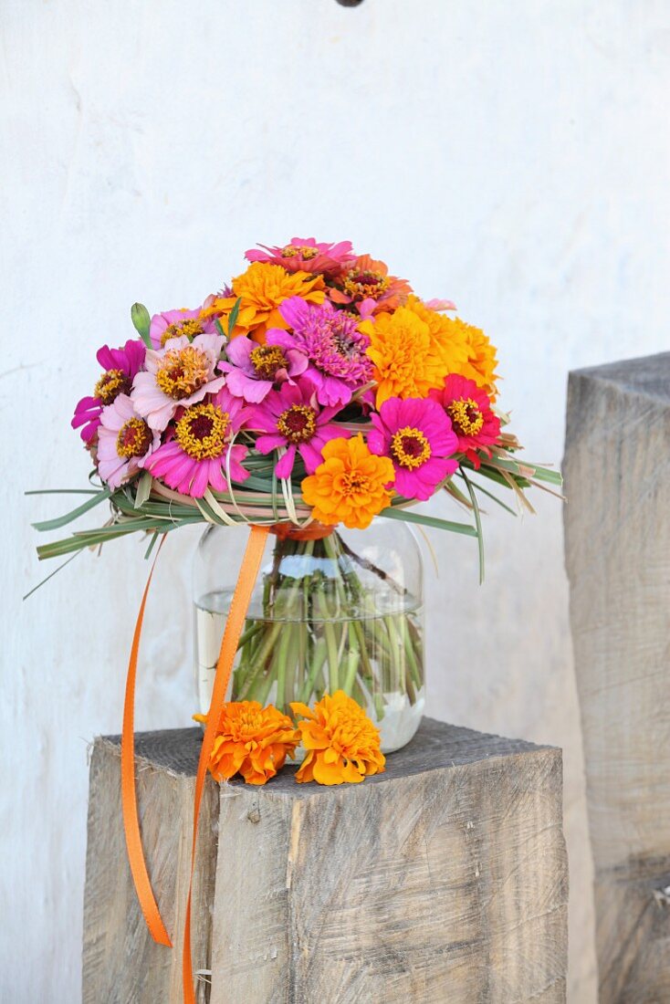 Colourful bouquet of zinnias and tagetes in glass vase on wooden block