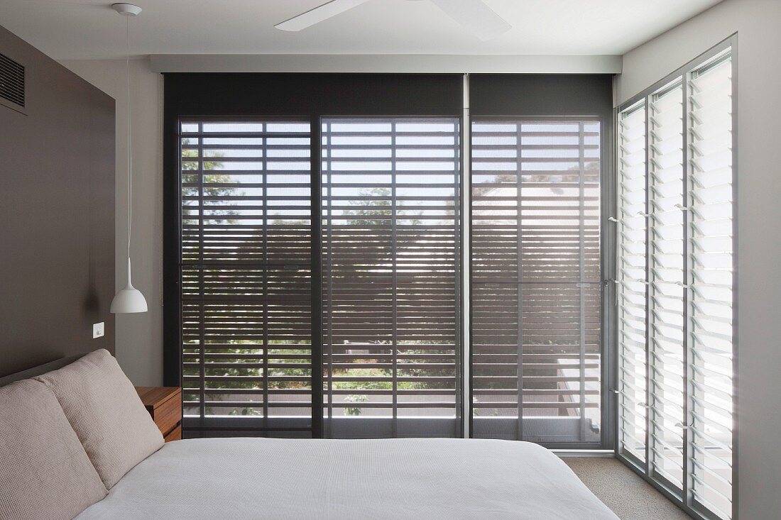 Bedroom with sunshades on glass walls and double bed against dark brown wall
