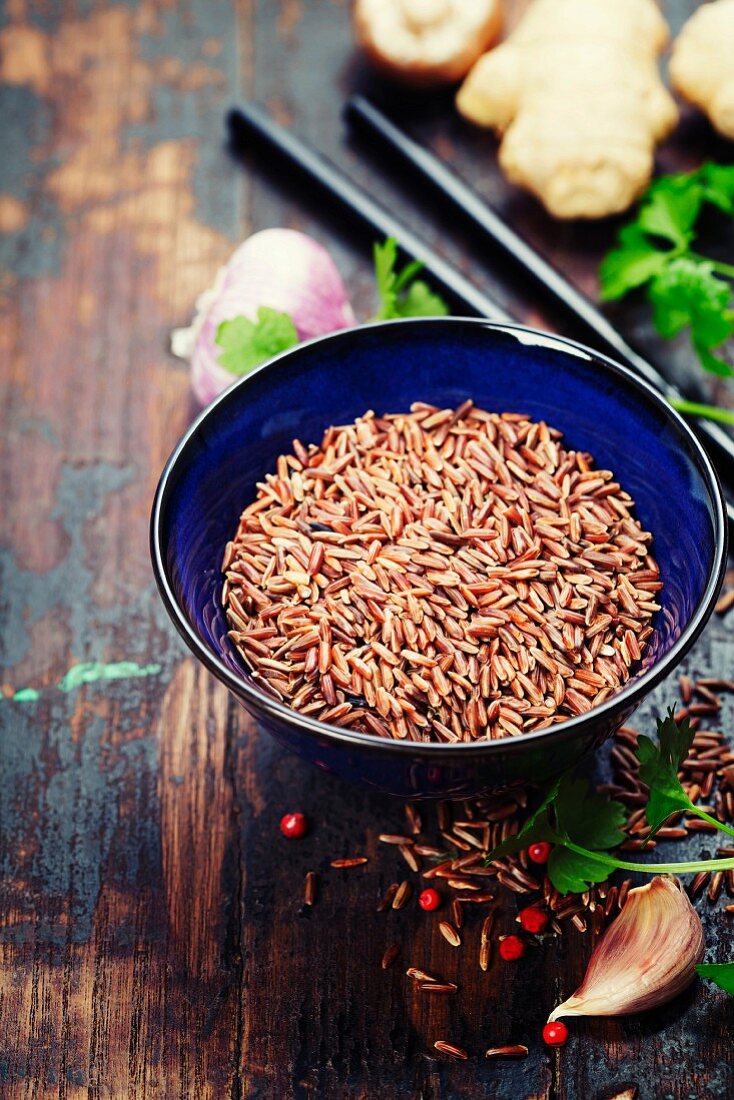 Roter Reis in einer Keramikschale und asiatische Zutaten auf Holzuntergrund