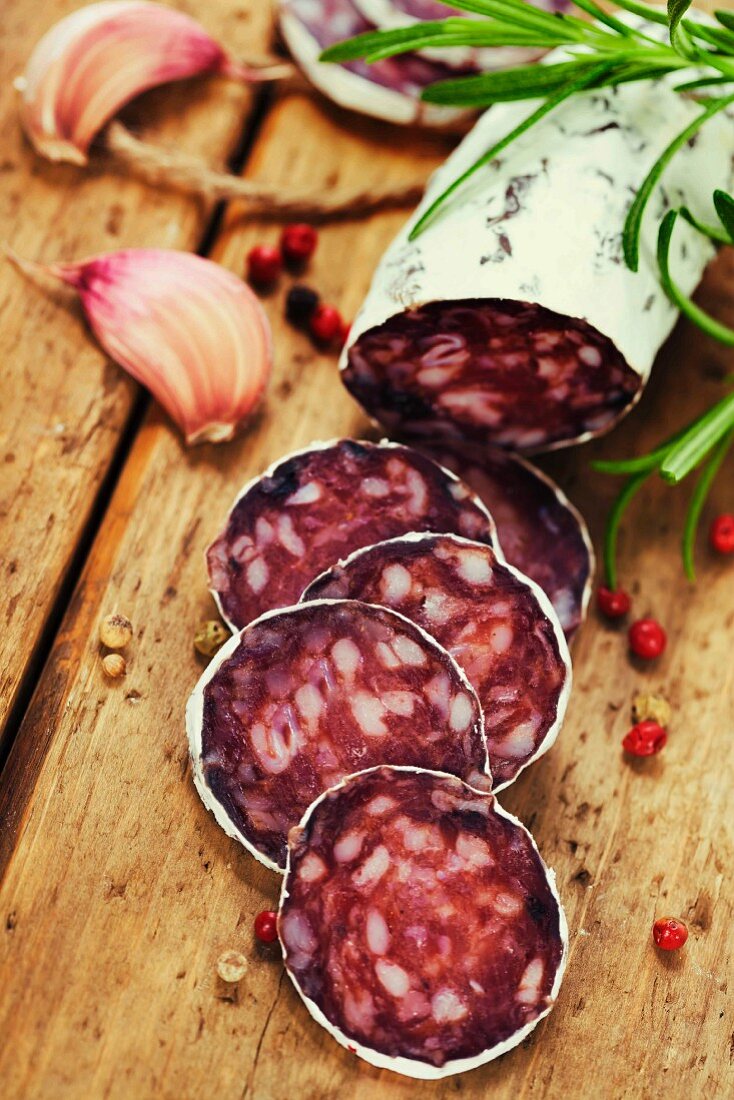 Salami teils in Scheiben geschnitten, auf Holzbrett mit Knoblauch und frischen Kräutern