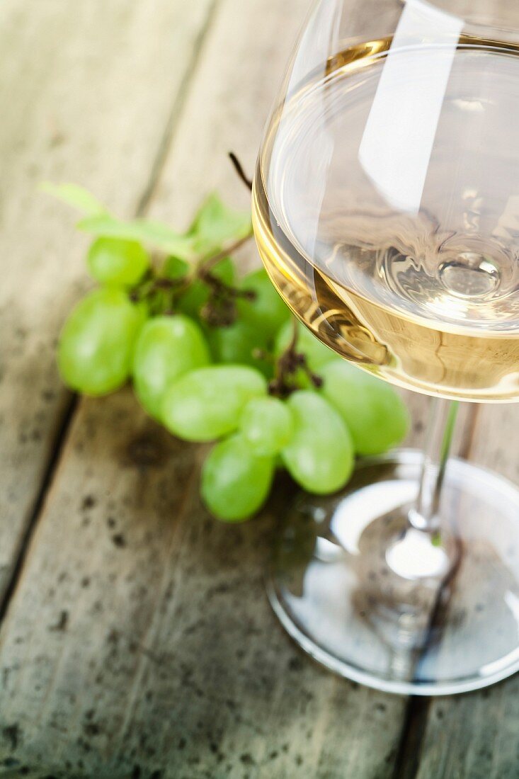 Ein Glas Weißwein und Trauben auf Holztisch
