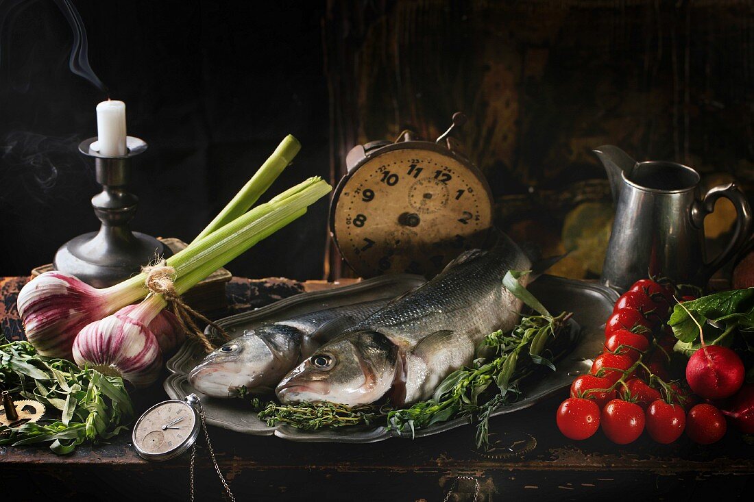 Stillleben mit rohem Seebarsch, Kräuter, Gemüse und Vintage-Uhr