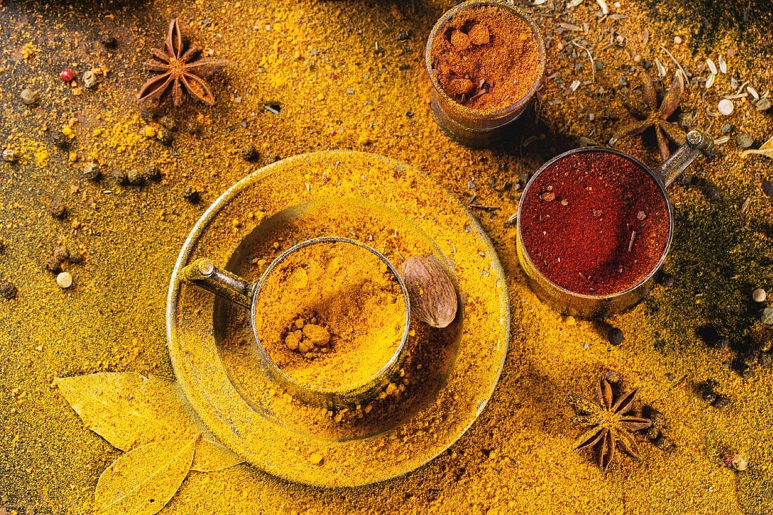 Verschiedene Gewürze Pfeffer, Kurkuma, Anis, Koriander in Vintage-Metallbecher, bestäubt mit gelbem Currypulver