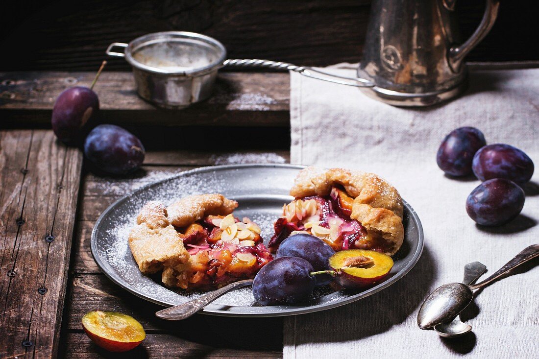 Galette cake with plums, served in vintage metal plate over old wooden table