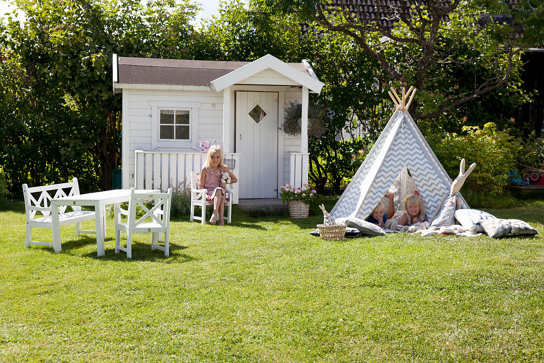Spielhaus, Tipi und Kindermöbel auf dem Rasen im sonnigen Garten