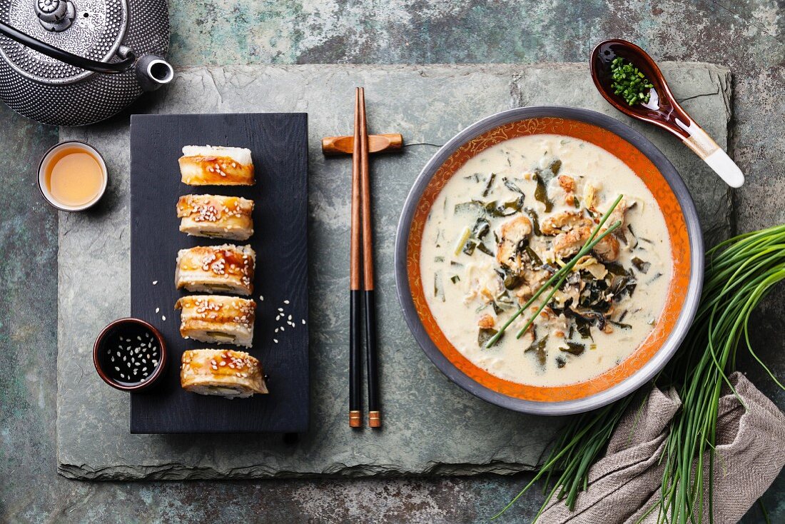 Creamy soup with Eel and sushi rolls on stone slate background