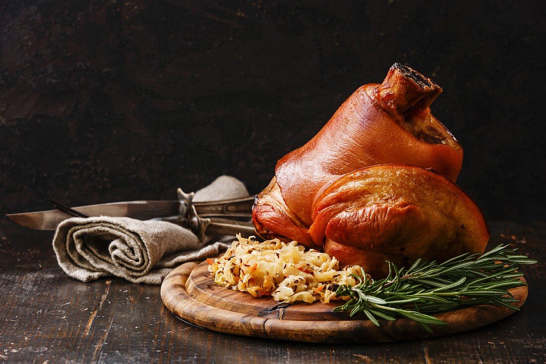 Roasted pork knuckle eisbein with braised boiled cabbage and rosemary on wooden cutting board