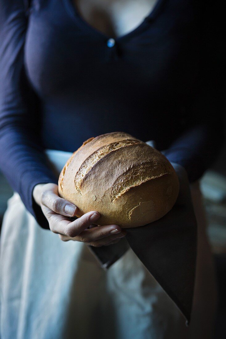 Frau hält frisch gebackenen Brotlaib in den Händen