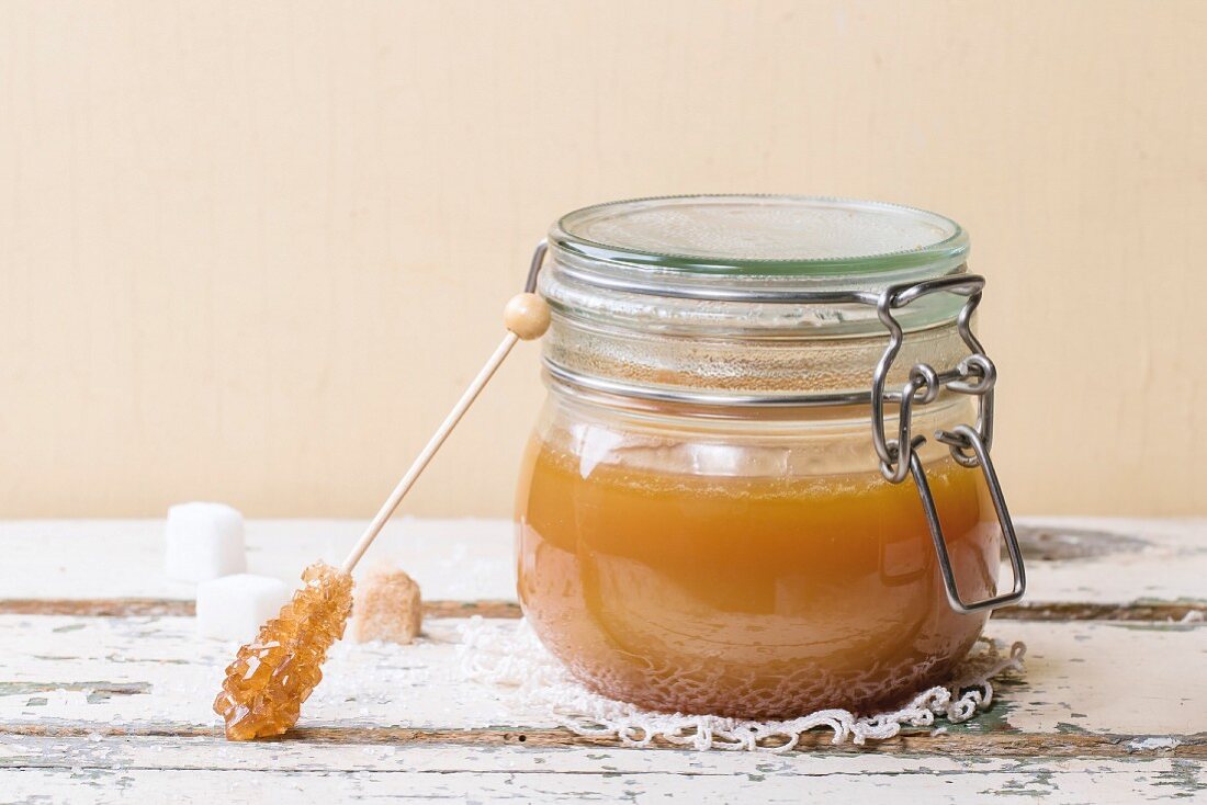Jar of homemade caramel sauce, served with sugar cubes over wooden table
