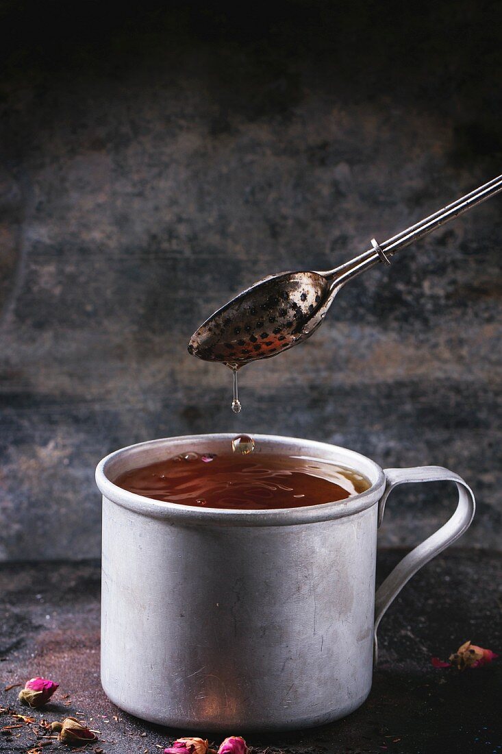 Heisser Tee in Vintage-Aluminiumbecher mit Tee-Ei und Rosenknospen