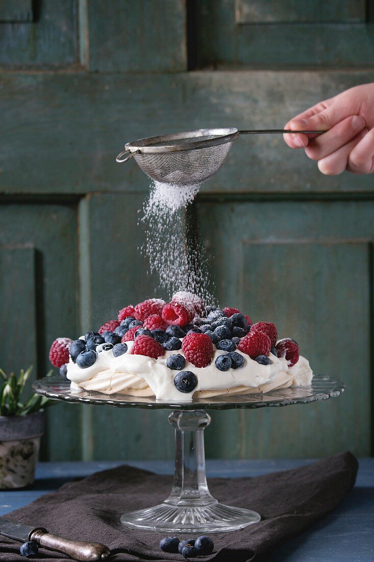 Vintage cake stand with Meringue dessert Pavlova with fresh blackberries and raspberries, strewing by sugar powder